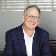 A man with white hair wears glasses and a blue suit.