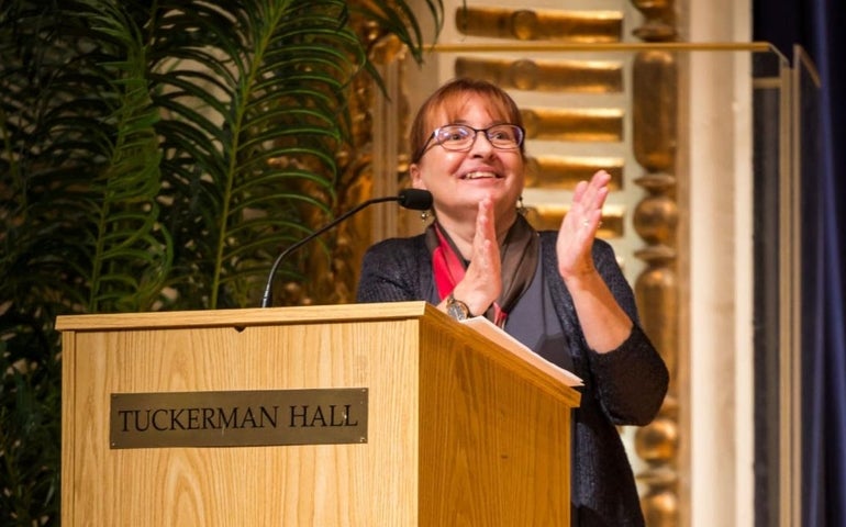 A woman with glasses claps her hands from behind a podium