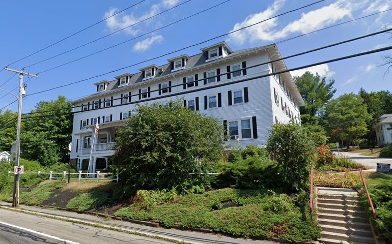 A large White Inn-style building sits on a hill with a small tree in front