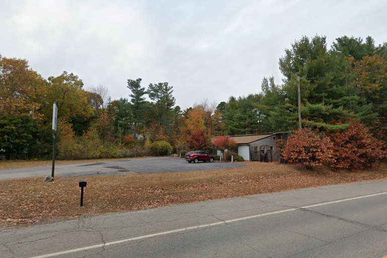 A small building with a car parked in a driveway in front