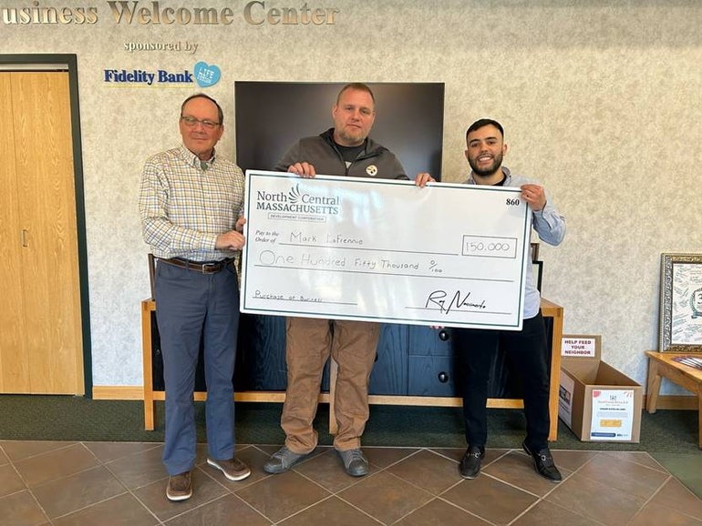 Three men stand side by side holding a large check