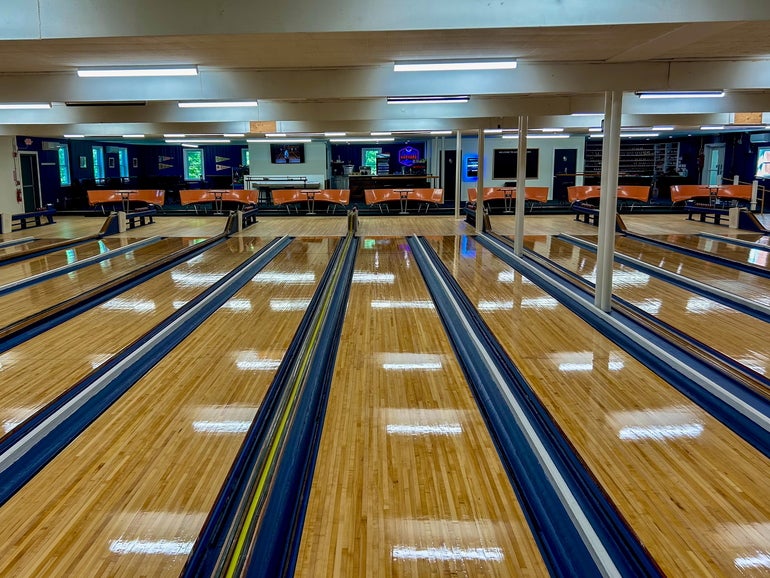 A shot of candlepin bowling lanes, facing the bowling area. Seats and a concession stands sit behind.