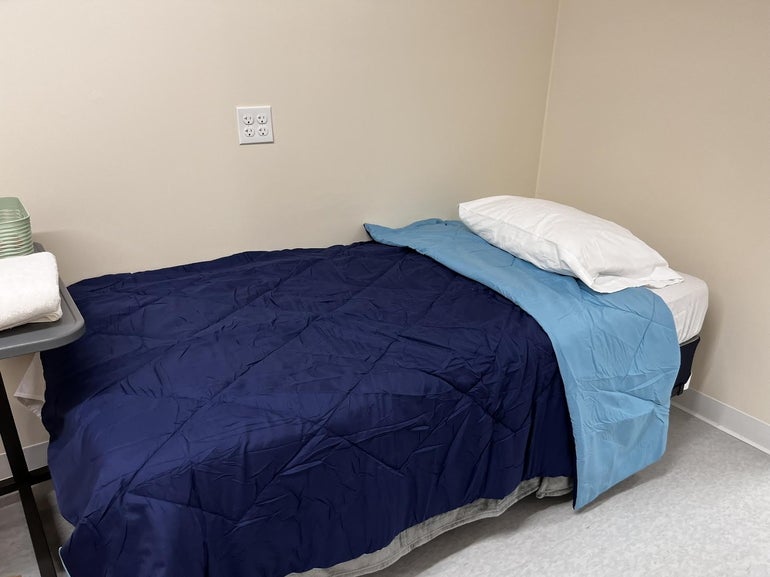 A bed with a white pillow and dark blue blanket, folded over at the top to show a light blue side of the blanket.