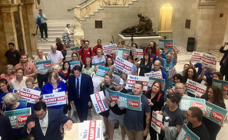 A group of protesters stand with signs inside a marble hallway.