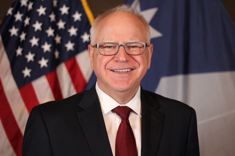 A man in a suit with glasses and an American flag behind