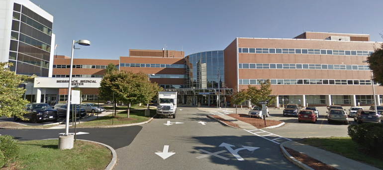 A brick hospital sits behind a parking lot.