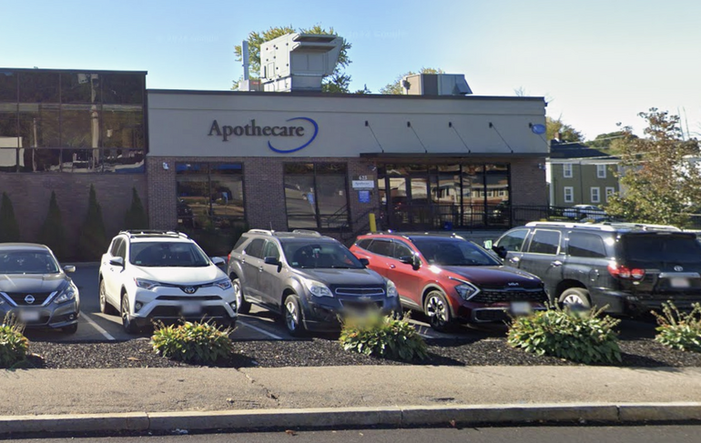 A brich building with windows in the front sits behind parked cars in a parking lot.