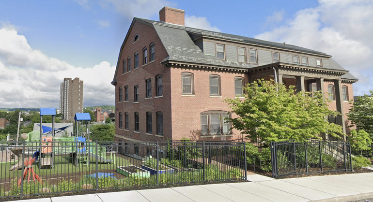 A children's playground sits the the left of a large brick building.