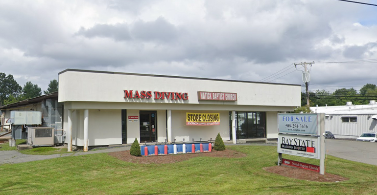 A one-story retail building with a lawn and sign in front