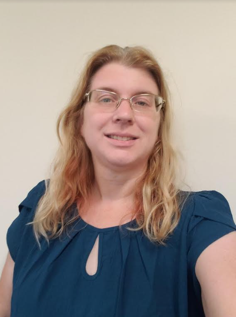 A woman with long blonde hair wears glasses and a dark blue blouse.