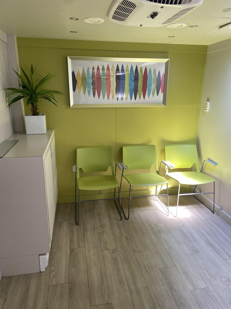 A small room with three green chairs and light wooden flooring. 