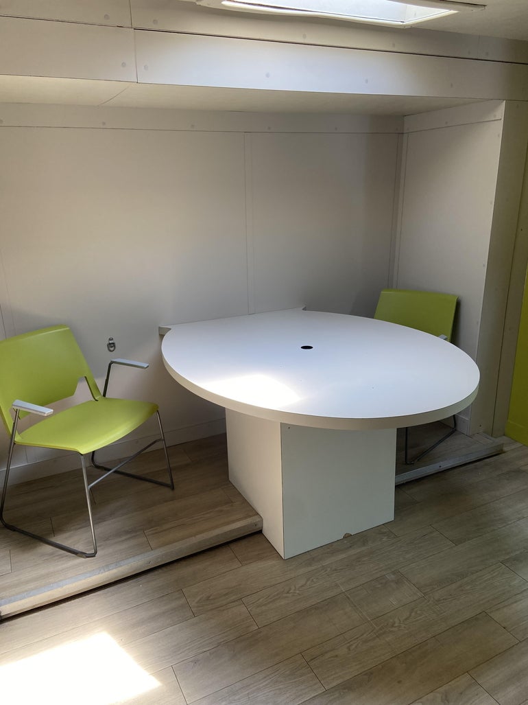 A white table attached to a wall with two green chairs on either side.