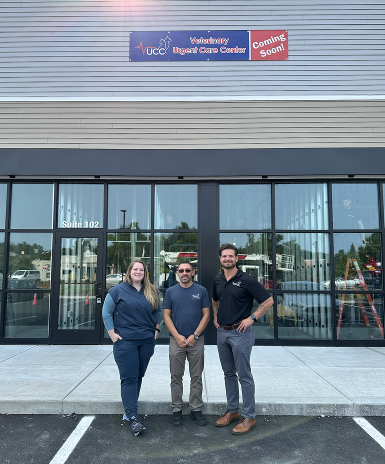 A woman and two men stand side by side in front of a glass storefront.