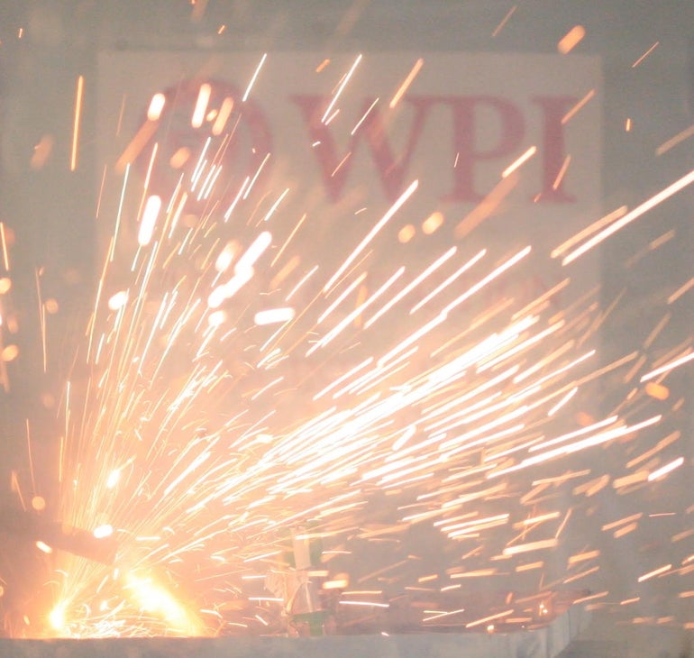 A white sign with "WPI' printed in red lettering with sparks flying in front of it