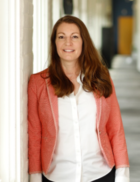 A woman in a red jacket and white shirt leans against a wall