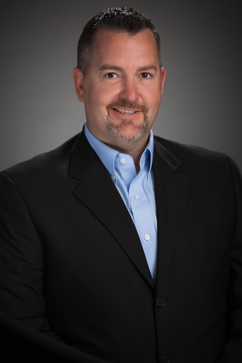 Headshot of a man with a goatee wearing a black suit jacket and light blue button down