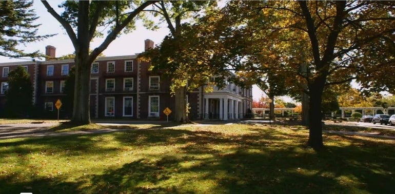 A brick hospital building sits behind a grassy lawn with trees.