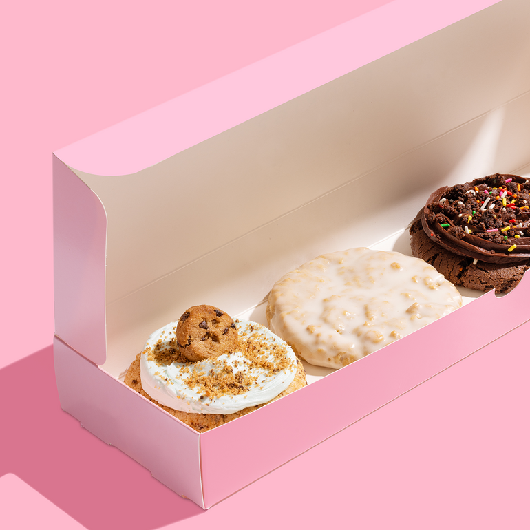 A pink takeout box with the lid open holds three cookies inside of it.