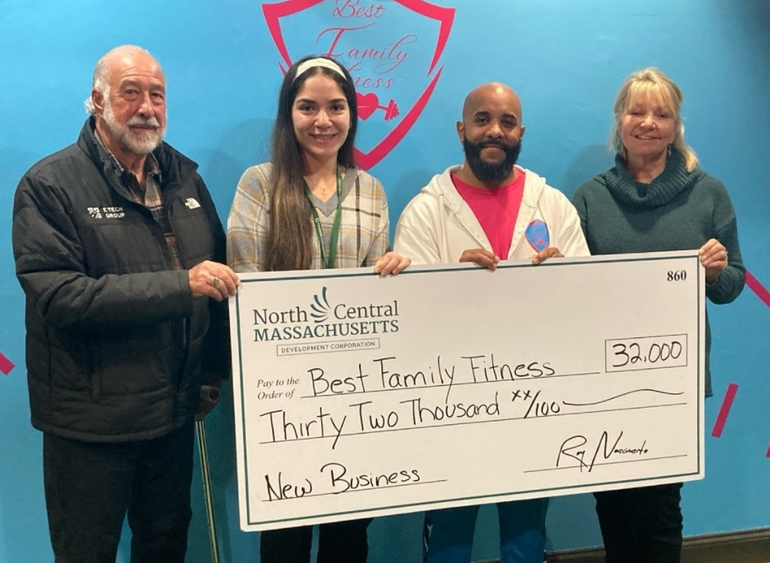 Four people stand side-by-side in front of a blue wall holding a large check for $32,000.