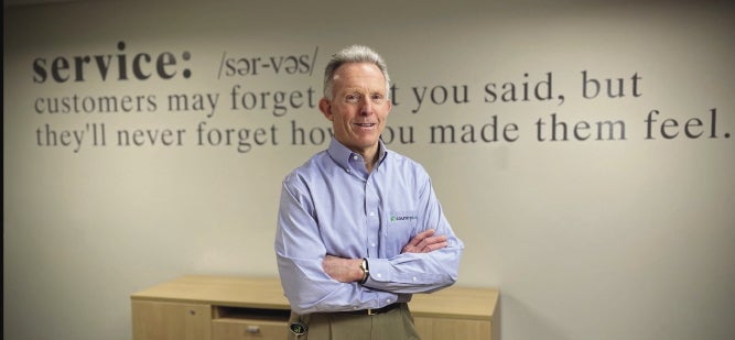 A man in a dress shirt stands in front of a word mural