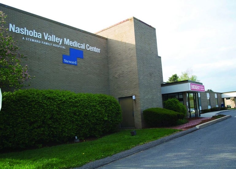 A brick building with "Nashoba Valley Medical Center" printed on the sign along a concrete driveway.