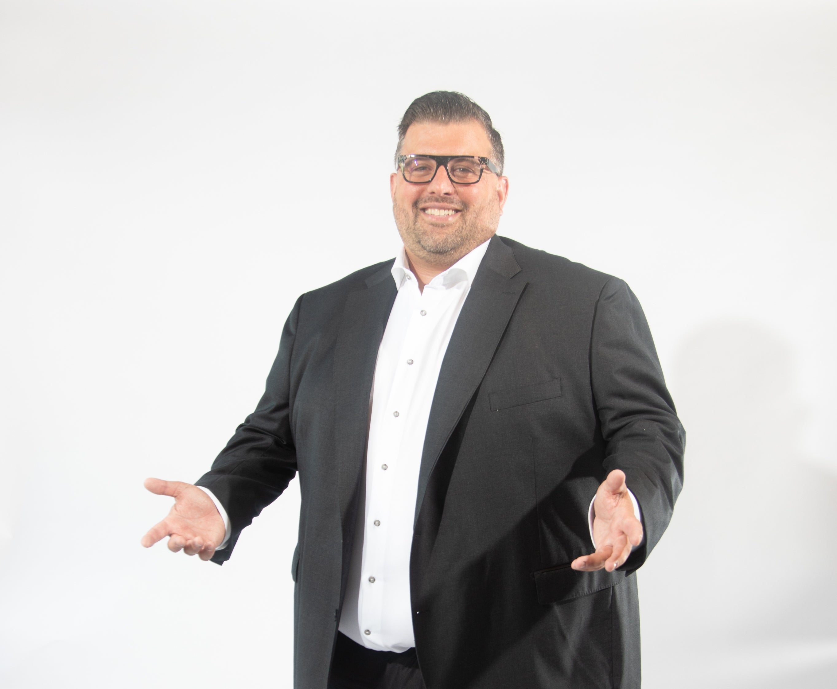 A man in a black suit smiles and shrugs