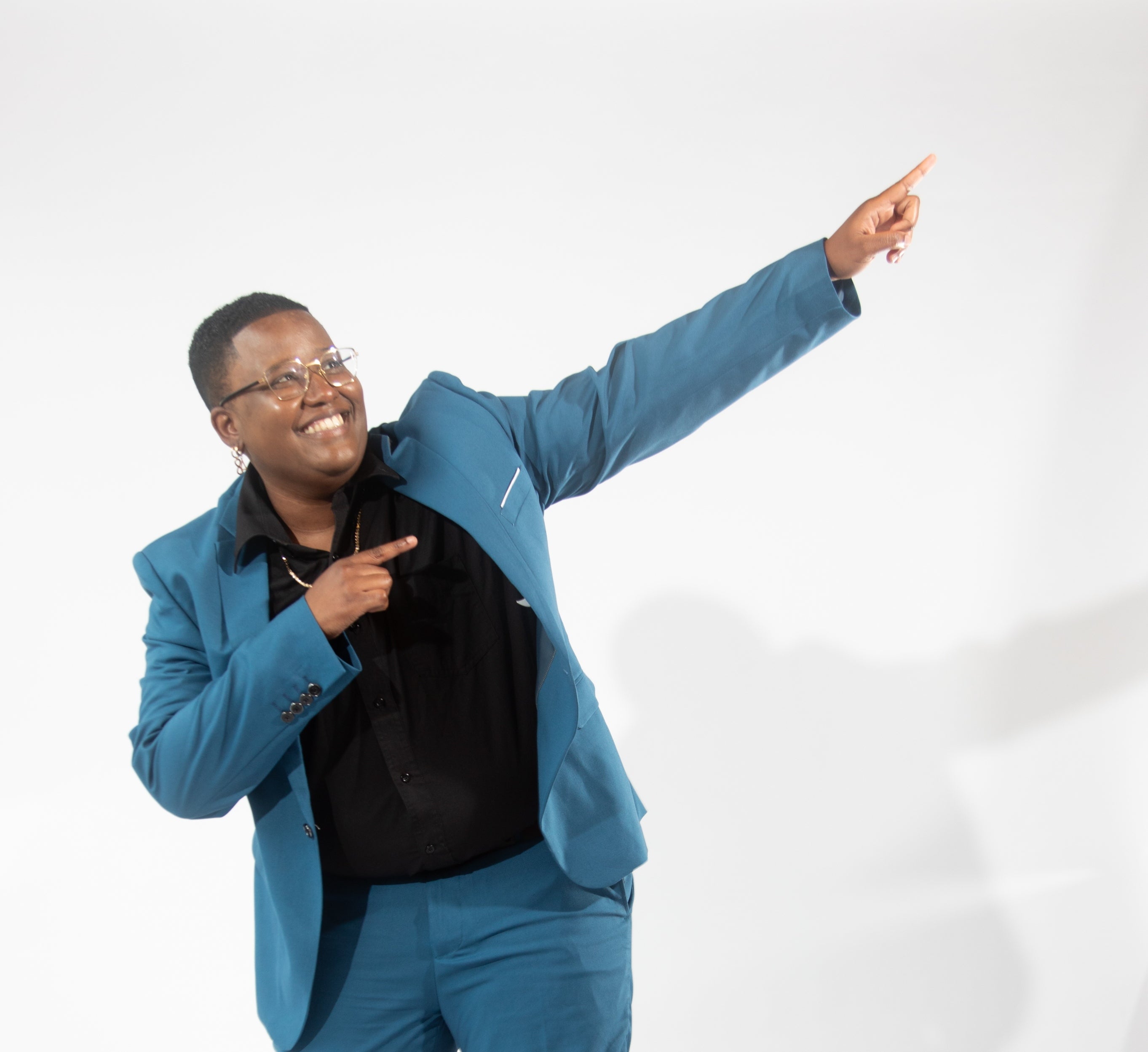 A woman with glasses in a blue suit points upwards and to the right with a smile on their face