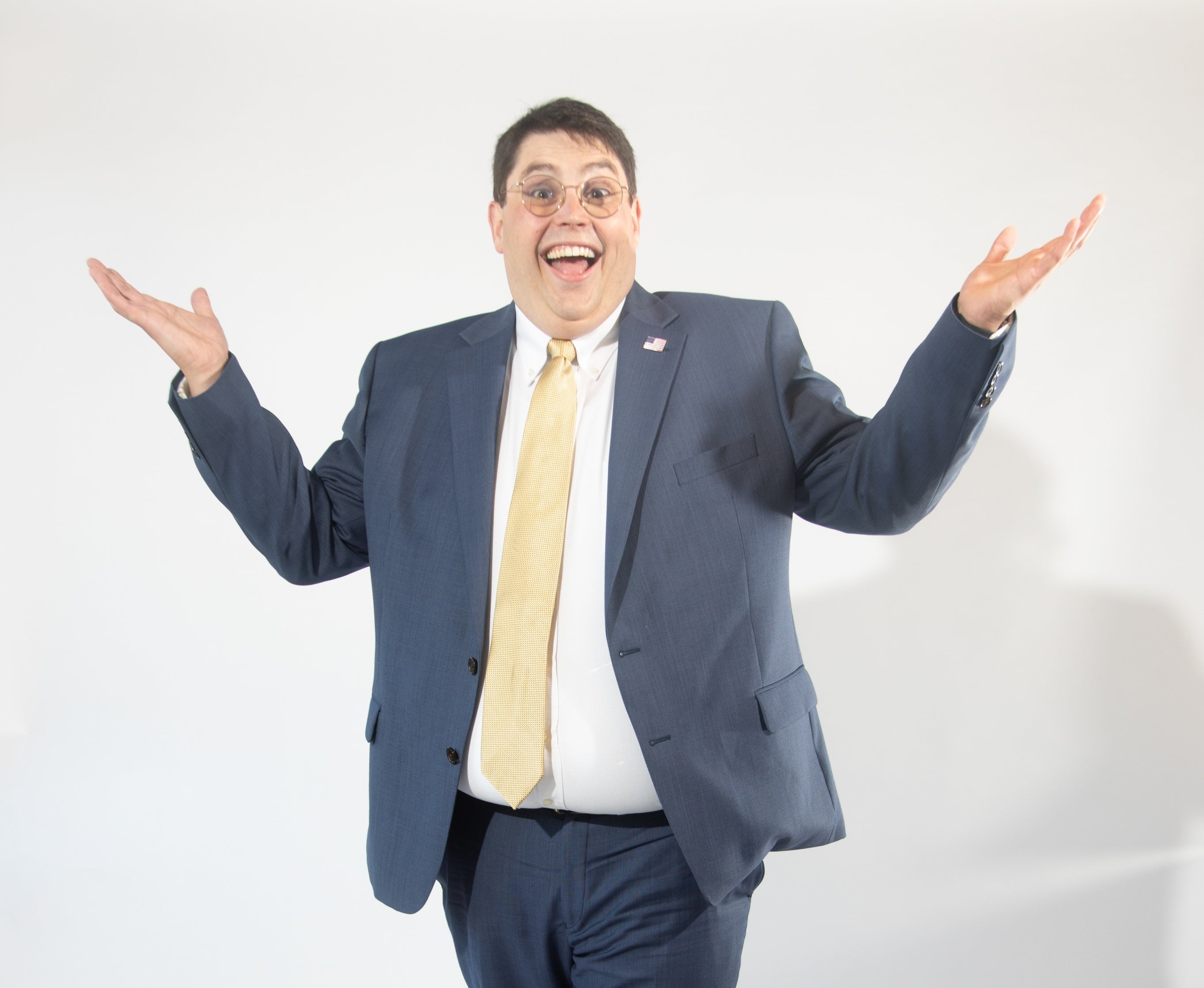 A man with glasses shrugs while smiling in a suit