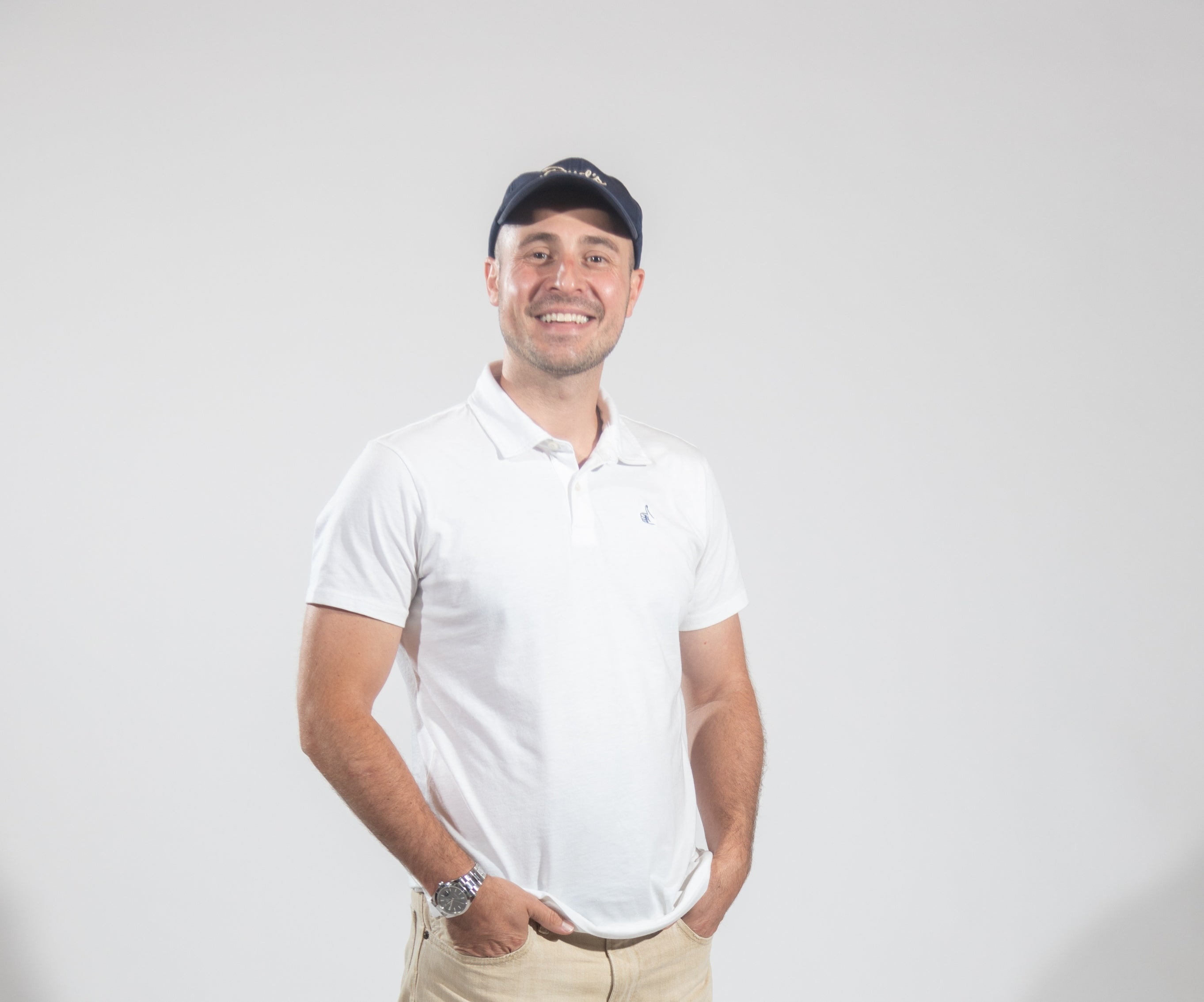 A man in a baseball hat and white polo with his hands in his pockets