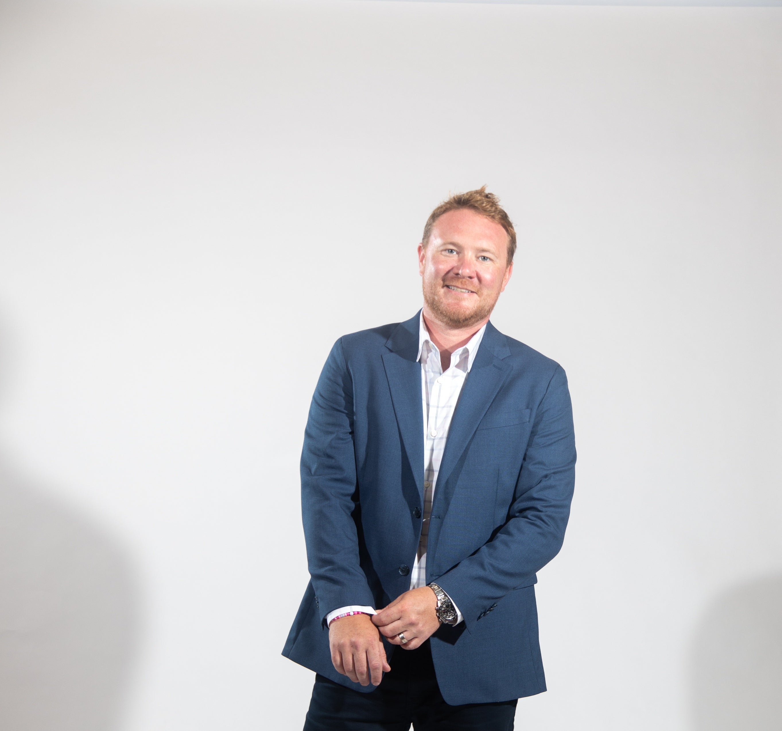 A man in a suit smiles as he adjusts his sleve