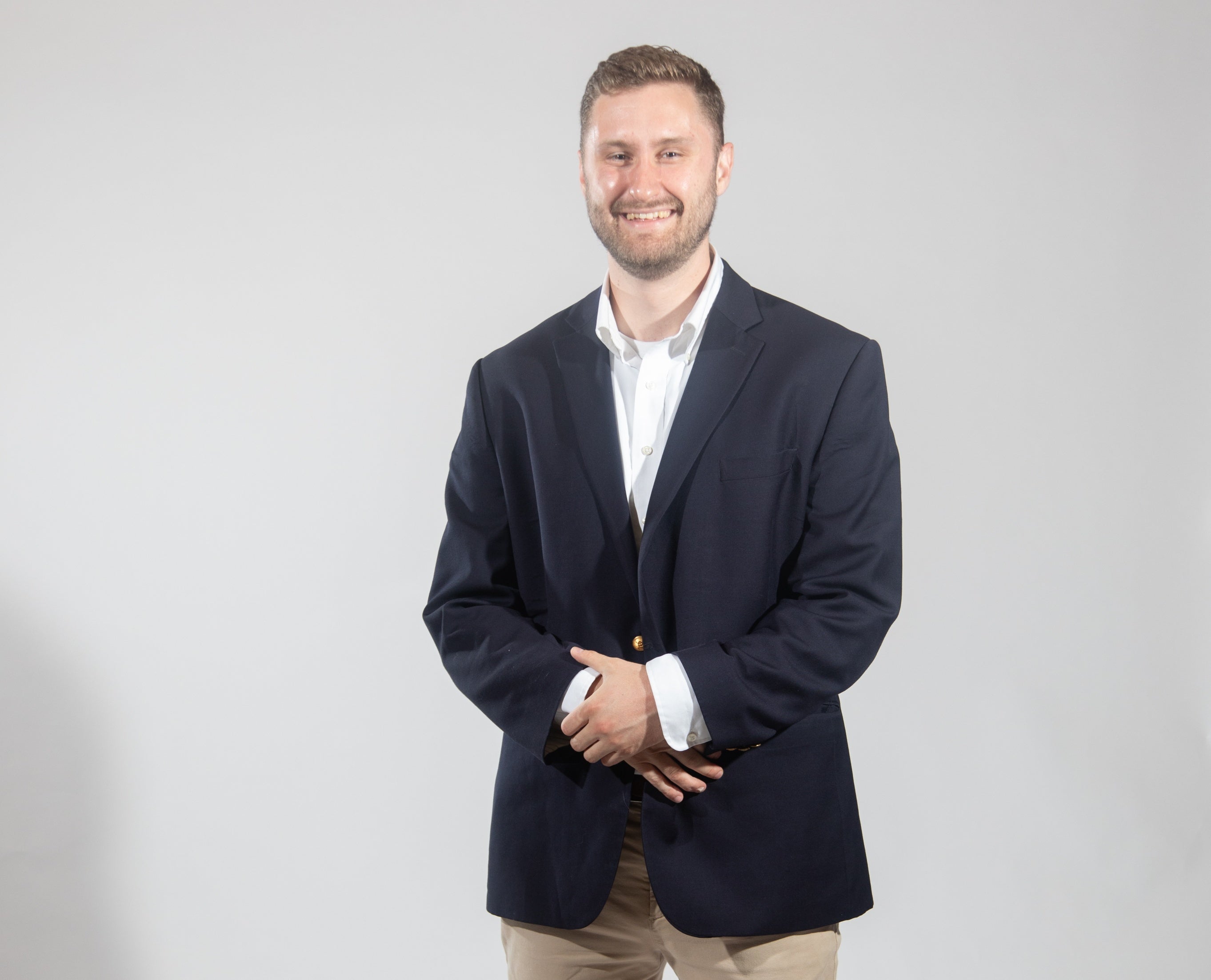 A man wears a black suit jacket, a white button down, and tan pants.