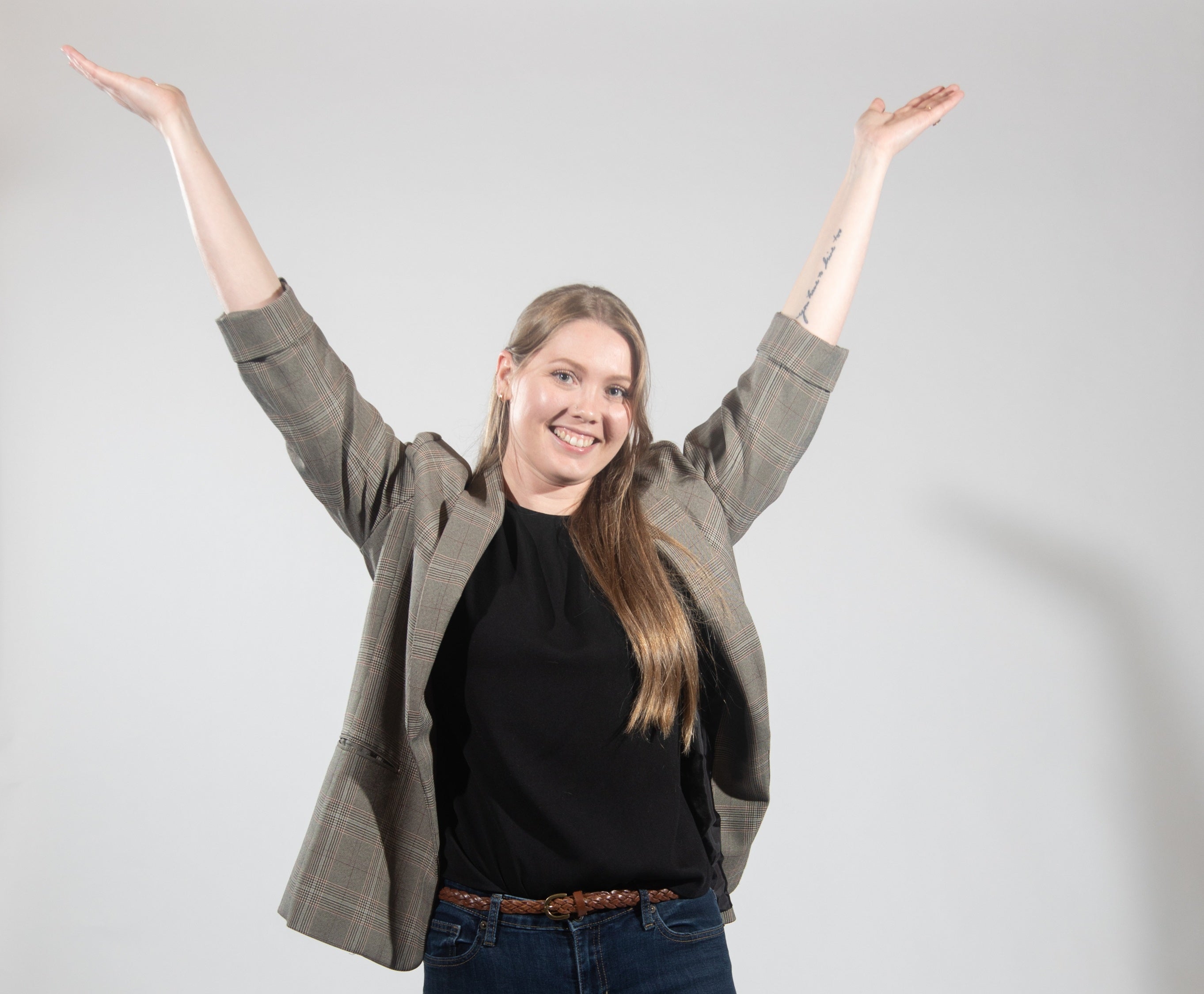 A woman in a grey suit jacket with her hands up in celebration