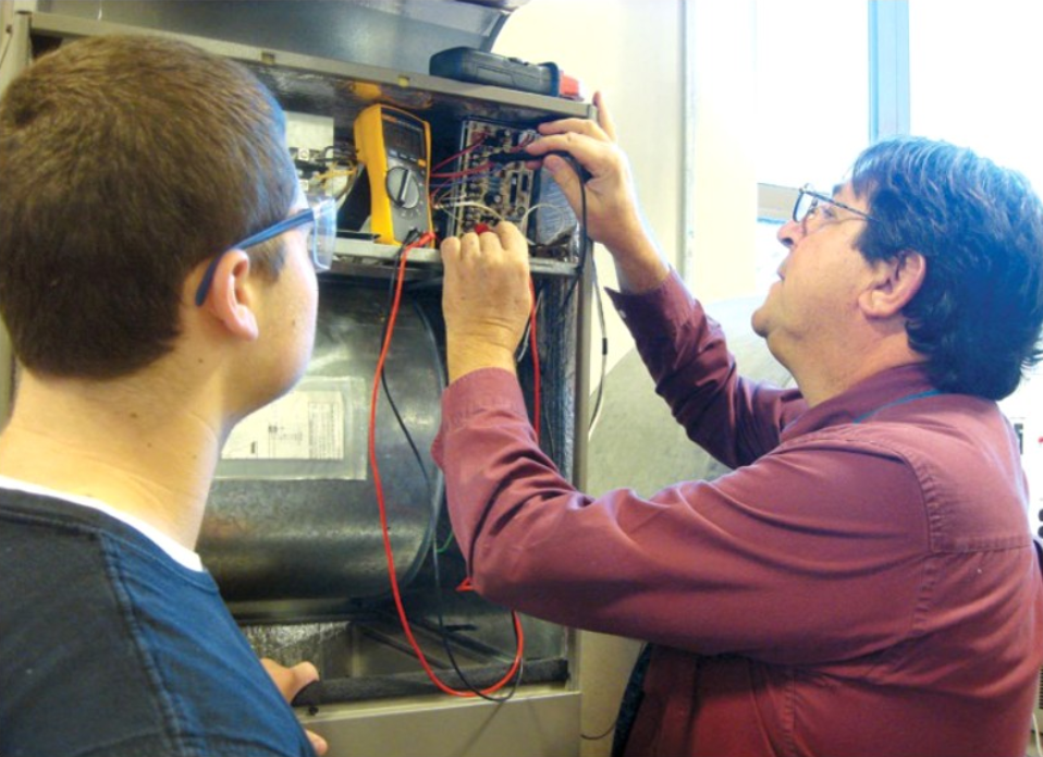 A younger person looks on as someone does work involving electrical wiring. 