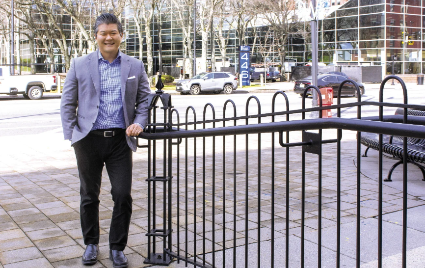 Man in suit leans on railing in front of city street