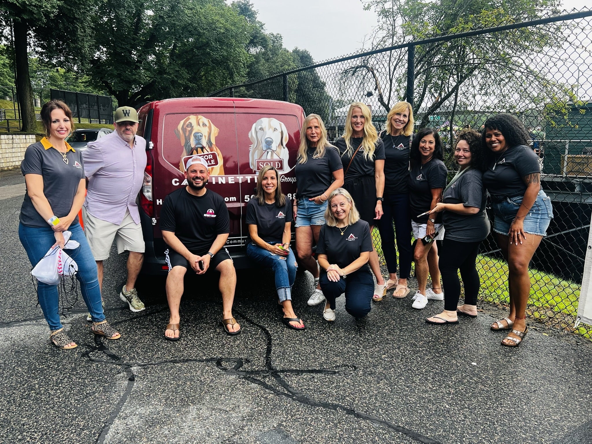 Eleven people stand and sit in front of a red mini van with drawings of dogs on it.