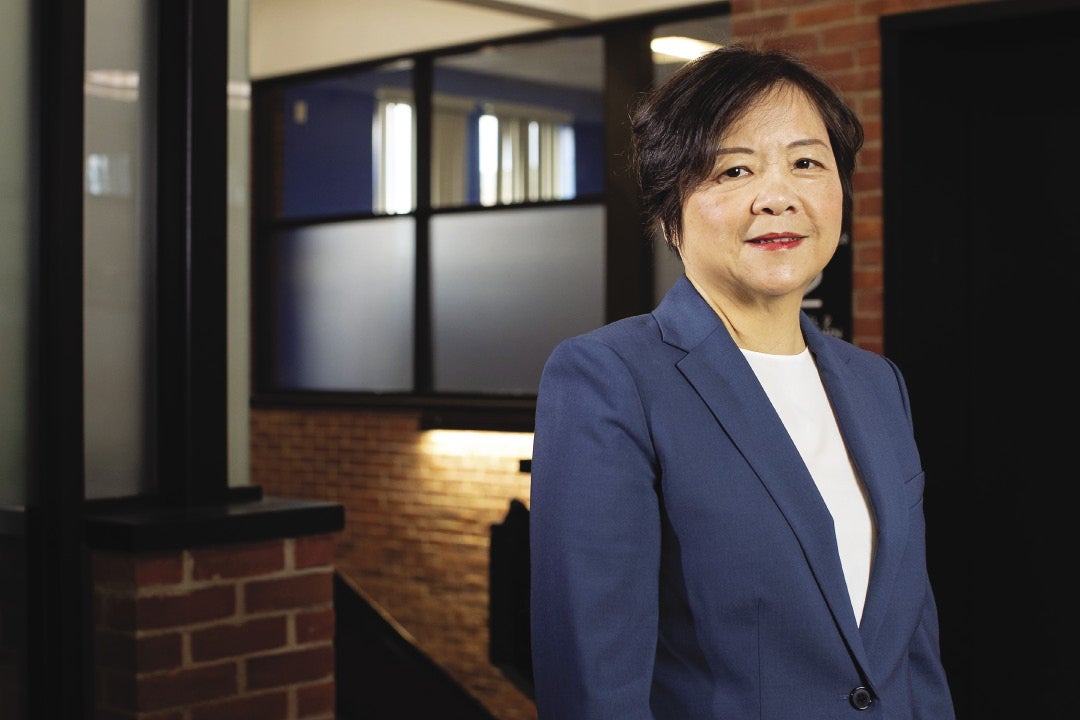 A woman with short dark brown hair wearing red lipstick, a dark blue suit jacket and white top.