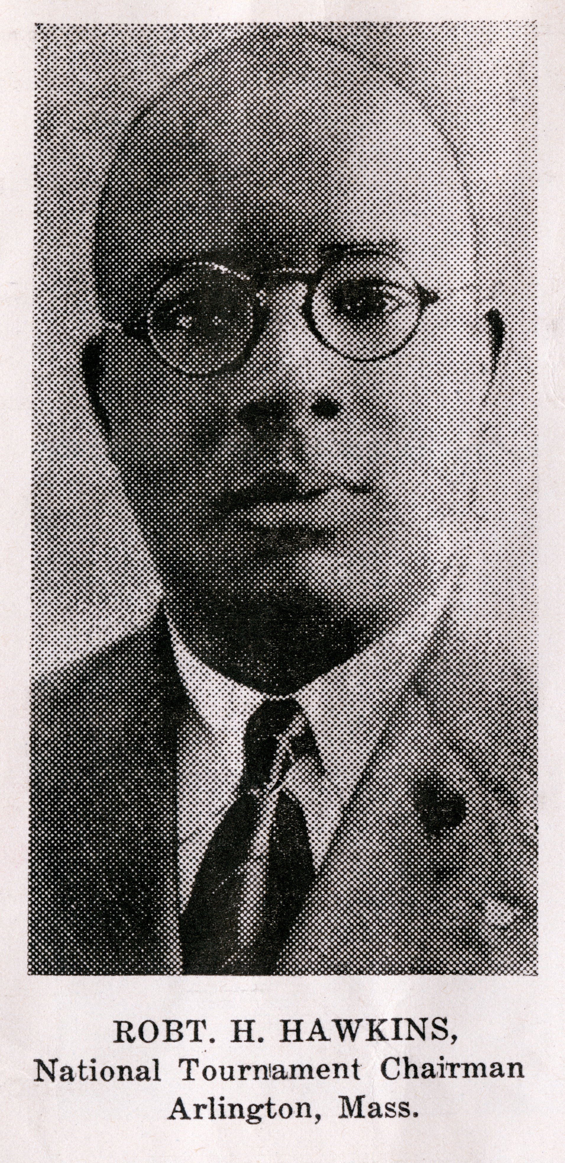 A black and white newspaper clipping of a headshot of a man wearing circular glasses and a suit with a tie