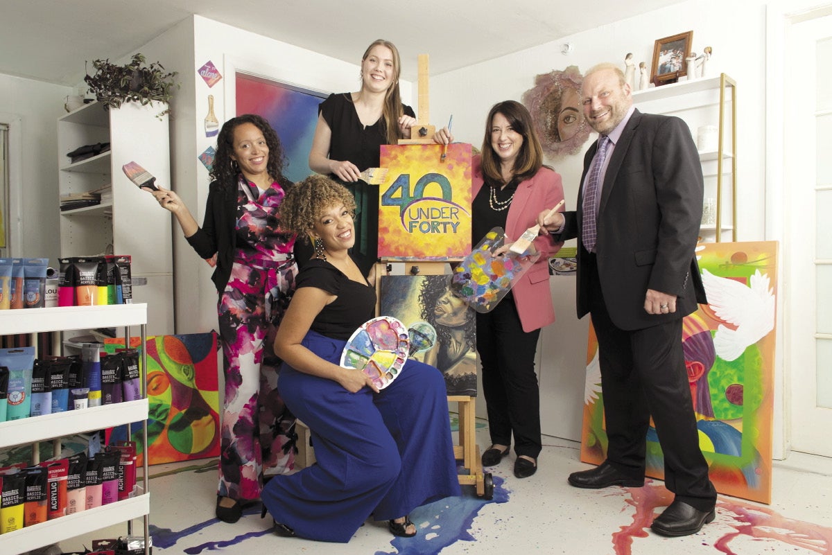 Four women and a man holding art supplies surround a painting with the 40 Under Forty logo on it.