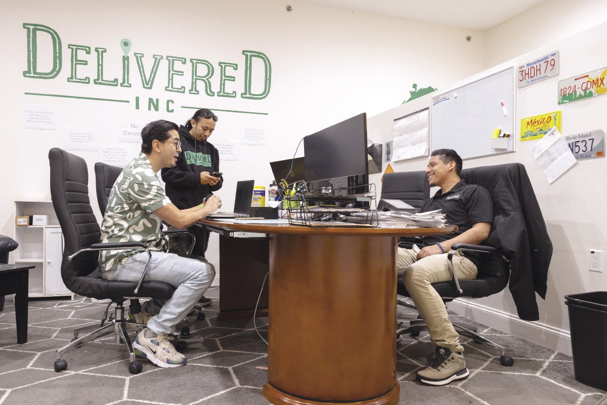 Three men sit at a desk