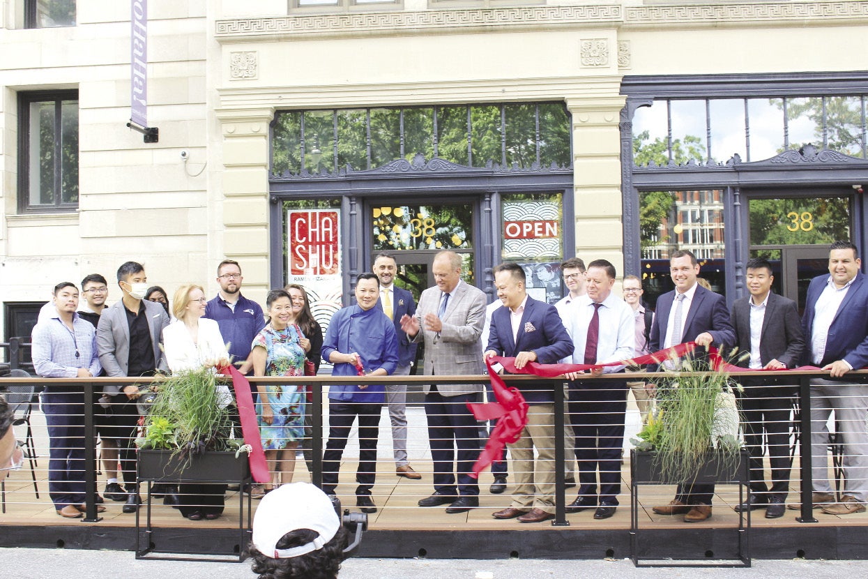 A group of people stand outside a restaurant cutting a red ribbon.