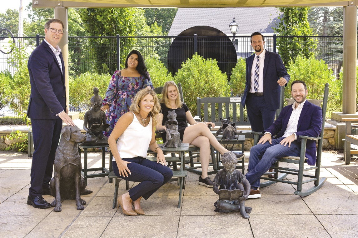 Three men and three women sit in the outdoor children's courtyard at Shrewsbury Public Library on a sunny day.