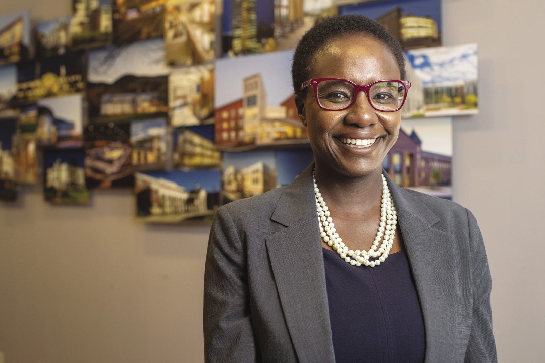 A woman with red glasses, a blue shirt, and a gray blazer smiles at the camera.