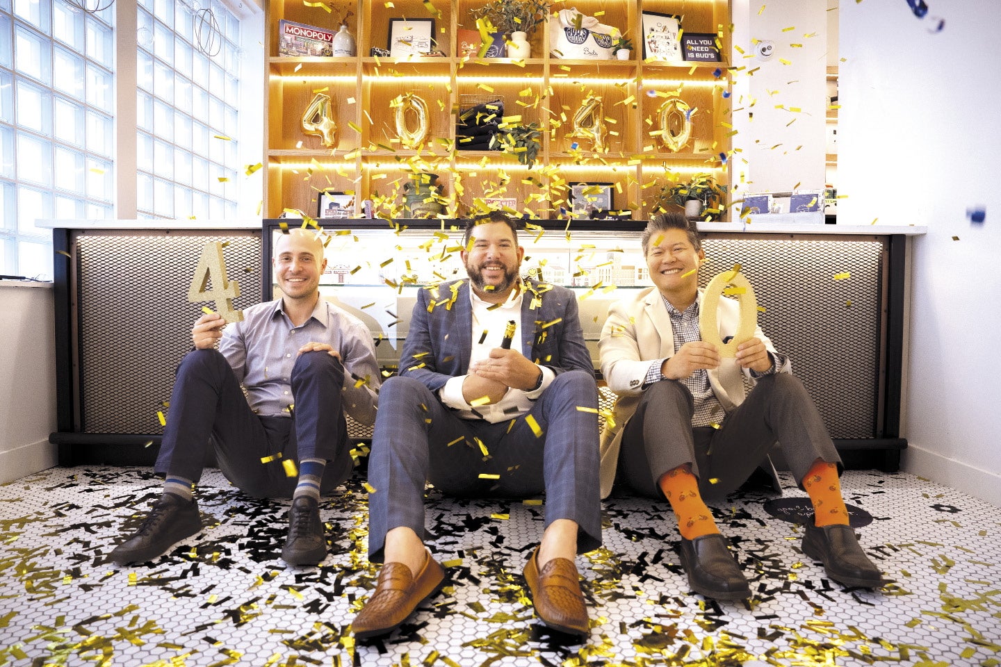 Three men sit on the floor of a cannabis dispensary as golden confetti surrounds them.