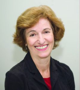 A woman with short blonde hair wears a black blazer and red top.